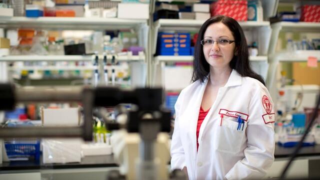 Polina Gross standing at a laboratory bench in a white lab coat.