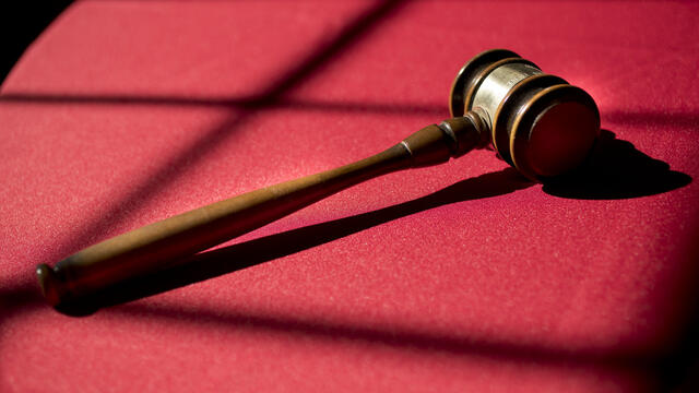 Image of a gavel placed on a table with red cloth.