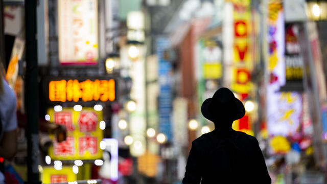 A figure silhouetted against illuminated street signs in Tokyo.