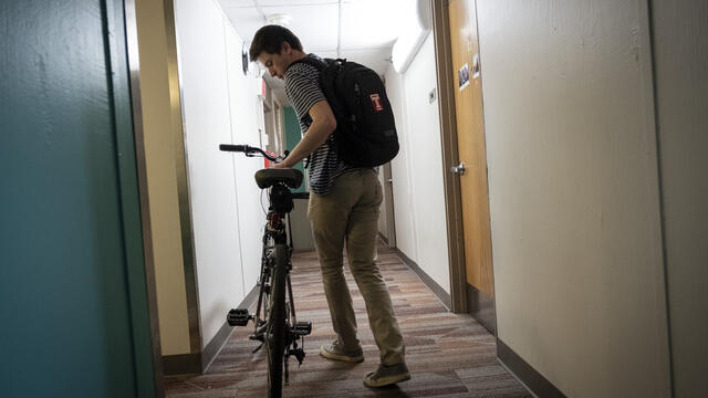 A student rolls his bike down the hallway of a residence hall