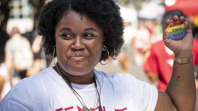 A Temple student holding up a rainbow colored pin that says