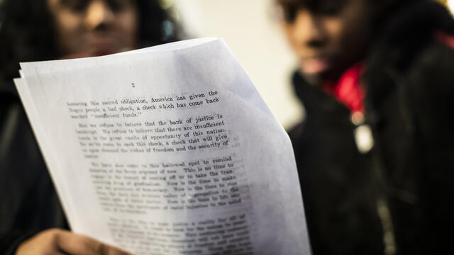 Two Black women read a page from a document together.