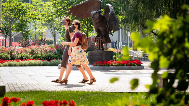 Two students wearing masks walk past an owl statue on Temple's Main Campus.