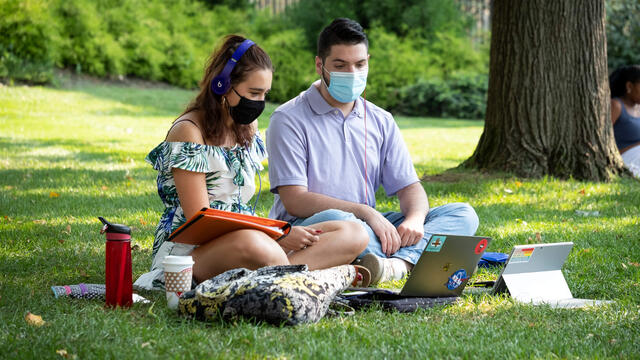 Two Temple students wearing masks study outside on Main Campus.