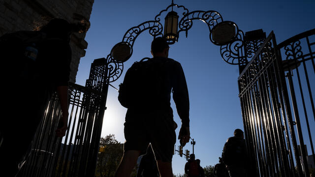 A student in silhouette walks through gates on Temple's Main Campus.