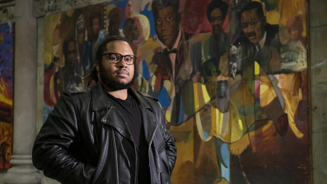 Tyler A. Ray stands in front of one of 14 murals inside the Church of the Advocate.