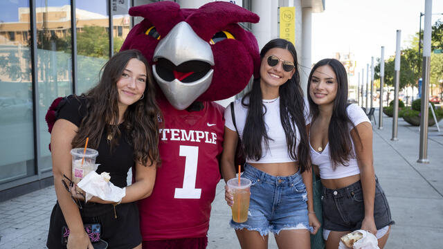 Three girls wearing T-shirts and shorts standing next to an Owl mascot.