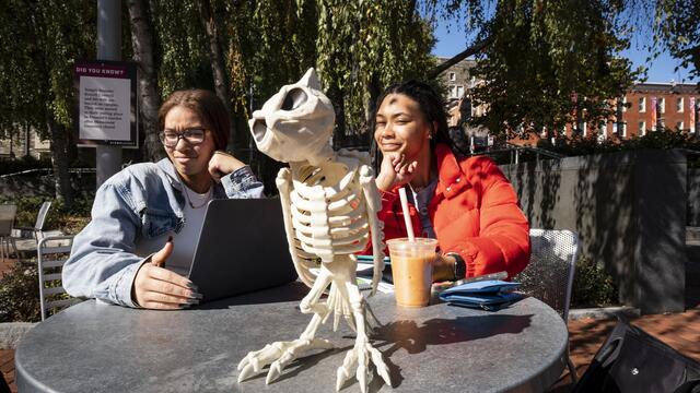 Two students sitting at a table outside with a skeleton