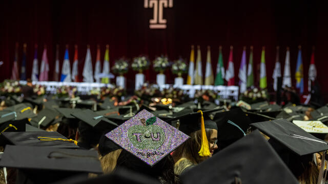 A crowd of graduates wearing caps looks towards the stage