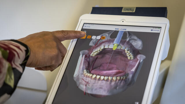 A finger points at a digital model of a mouth on a screen