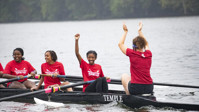 Image of children with smiles wearing red t-shirts, rowing a boat.