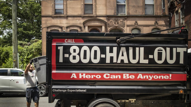 Image of a man wearing a gray shirt dumping trash in a pickup truck.