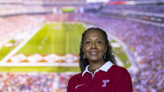 A woman wearing a cherry and white Temple shirt pictured with the background of Lincoln Financial Field.