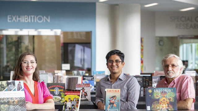 Professors Christina Baker, C sar Cabezas and Augusto Lorenzino standing in front of books on display in Charles Library for Hispanic Heritage Month
