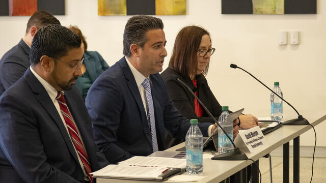 Individuals sitting at a table in front of small microphones