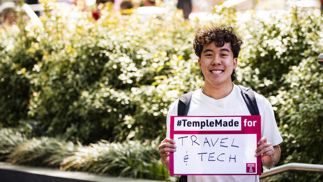 Image of Tran holding a sign that says #TempleMade for travel and tech