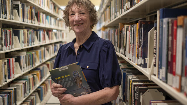 Sandi Thompson standing in the book stacks with a book in her hands at Ambler Campus Library