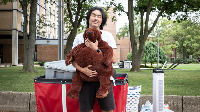 A student stands in front of J&H hugging a large stuffed bear.