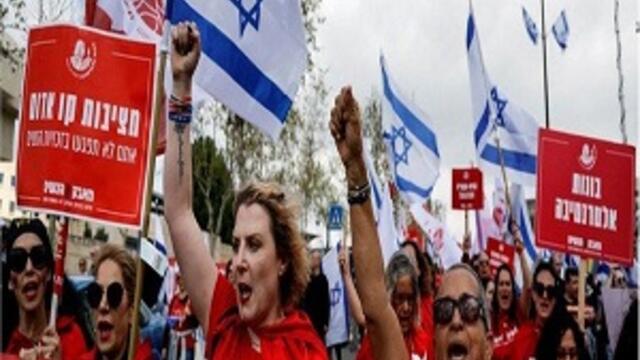 Israeli women protesters wearing red shirts and holding signs and the Israeli flag