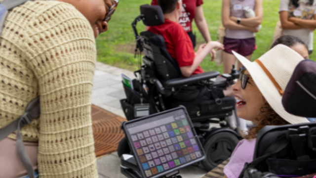 Students using AAC devices and wheelchairs mingle and chat outdoors on Temple's campus with others
