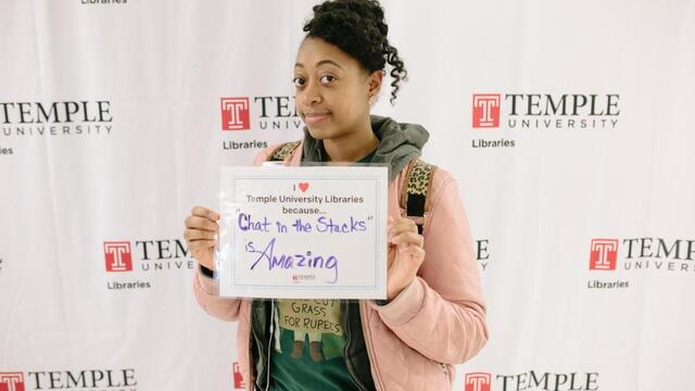 photo of Temple student with sign that reads: I love the Libraries because Chat in the Stacks is amazing.