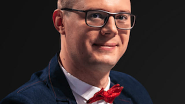 image of Dr.Maksym Yakovlyev wearing glasses, in a blue suit, white dress shit and red bowtie