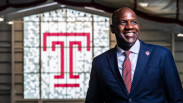 Arthur Johnson, in suit, smiling in front of Temple logo