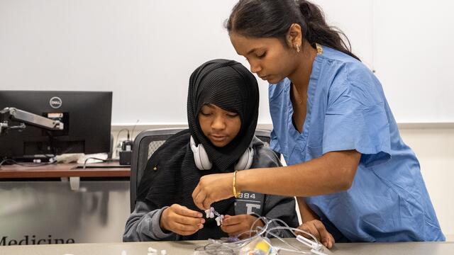 A medical student helps a middle school student perform an activity