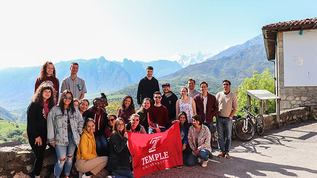 Mountains in the background, a group of Temple students holding a Temple cherry flag.