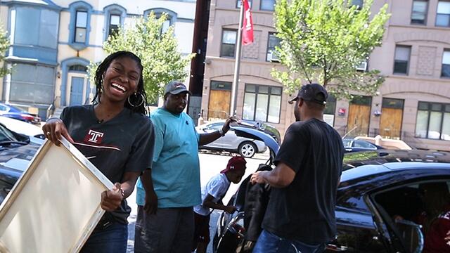 A woman in a Temple T-shirt smiling as she unpacks a car during move in.