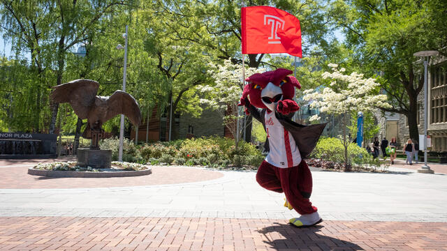 Hooter carries the Temple flag as he runs past the owl statue and points at the camera