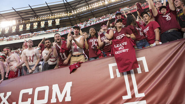 Image of Temple fans cheering on the Owls against Penn State at a football game. 