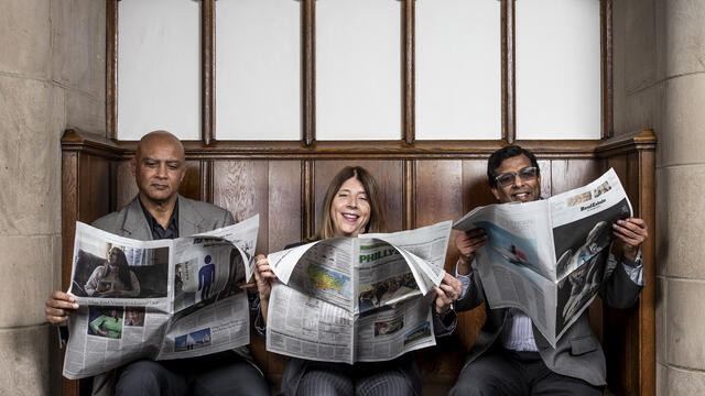 An image of the study's authors sitting on a bench reading newspapers.
