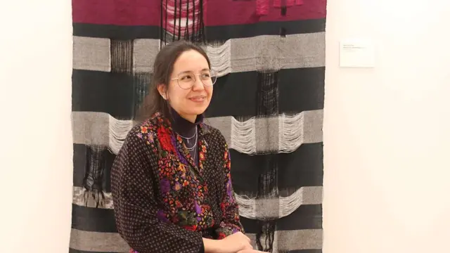 Artist Alicia DeVrio sits in front of her work