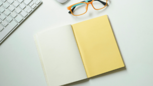 White and yellow notebook placed near keyboard and eyeglasses 