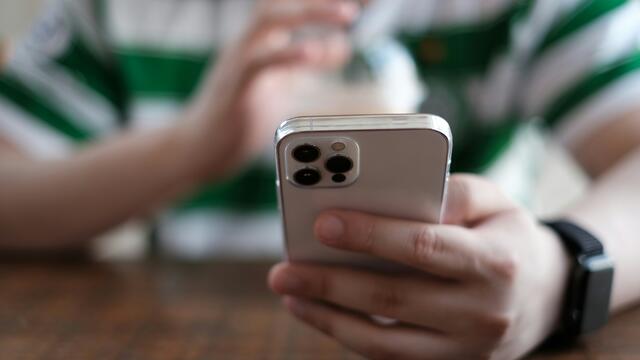 Person in a striped green shirt holding an iPhone