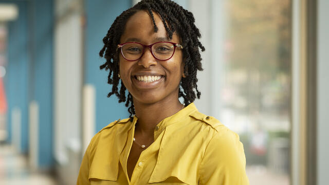 a professor in a yellow shirt standing before a window.