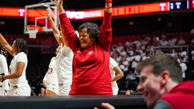 Image of Temple University s Coach Diane Richardson smiling and raising her hands during a college basketball game.