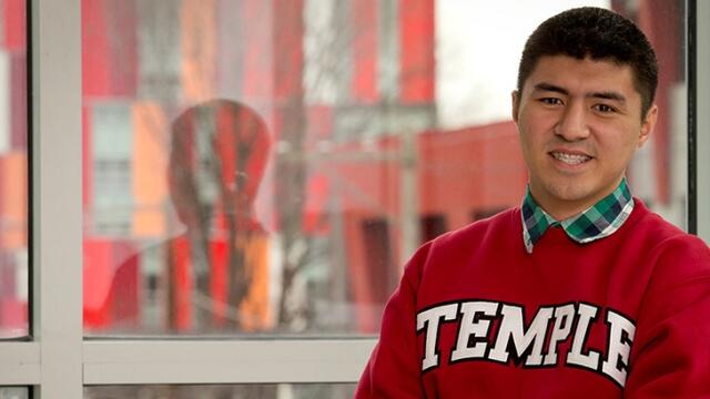 Matthew Velasquez standing in front of a window, wearing a cherry Temple sweatshirt.