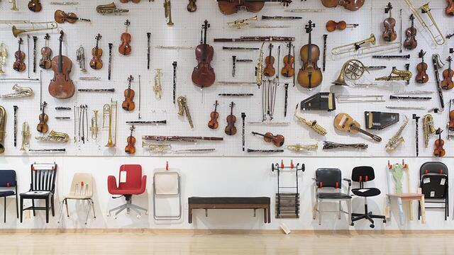 A large display of musical instruments and chairs hanging on a gallery wall.
