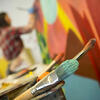 Paintbrushes and a woman painting in the background.