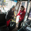 A young woman helping an older woman carrying a cart safely board a bus.