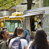 A crowd of people in front of a row of food trucks on campus.