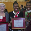 Two women holding awards and one woman holding flowers.