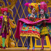 Three opera singers wearing brightly colored costumes and wigs performing on stage.