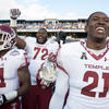 Temple football players smiling and celebrating on the field after a big win.