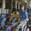 A man sitting amid cabinets, desks, chairs and other items in a warehouse.