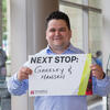A man in a blue shirt holding a sign that reads Next Stop: Greeley and Hansen.