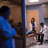 A physician watching two students work with a patient in a clinic room