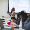 A woman in a red face covering standing before an overhead projector screen.